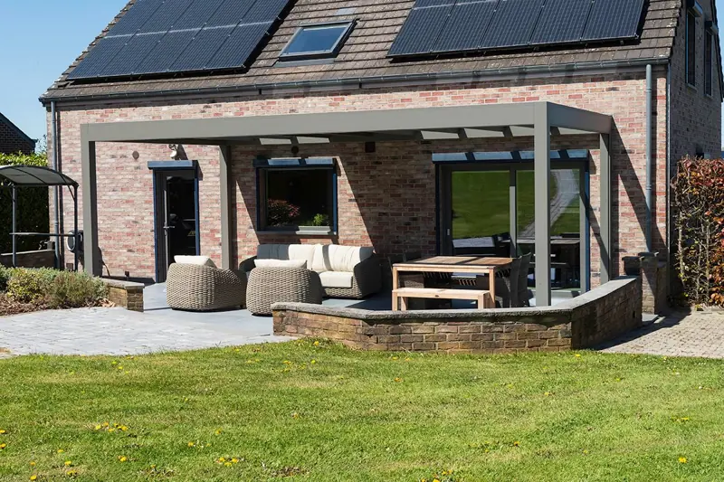 Pergola aluminium adossée à une maison en briques avec salon de jardin