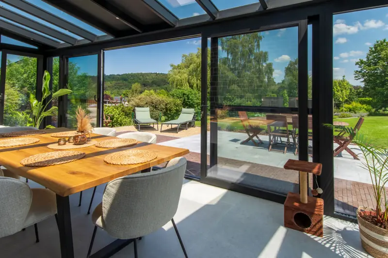 Véranda vitrée sur terrasse avec table en bois et vue sur la campagne