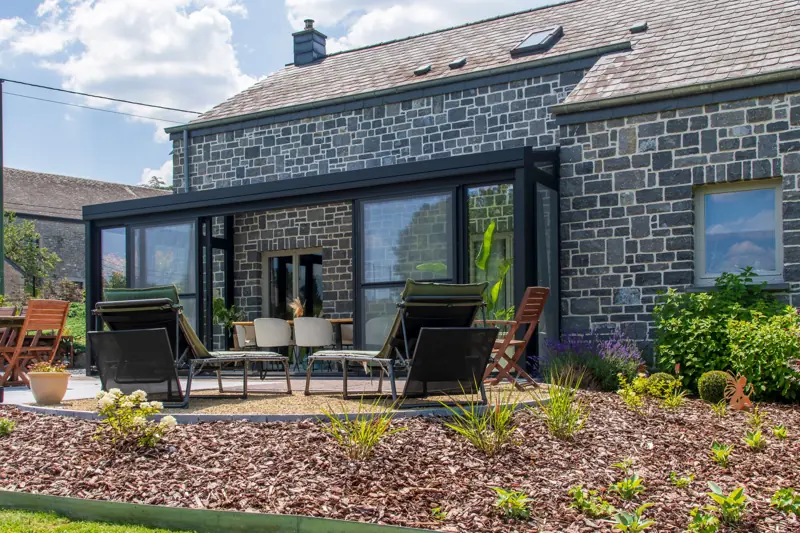 Véranda gris anthracite accolée à une maison en pierre