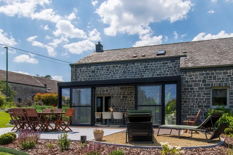 Véranda moderne accolée à une maison en pierre avec terrasse